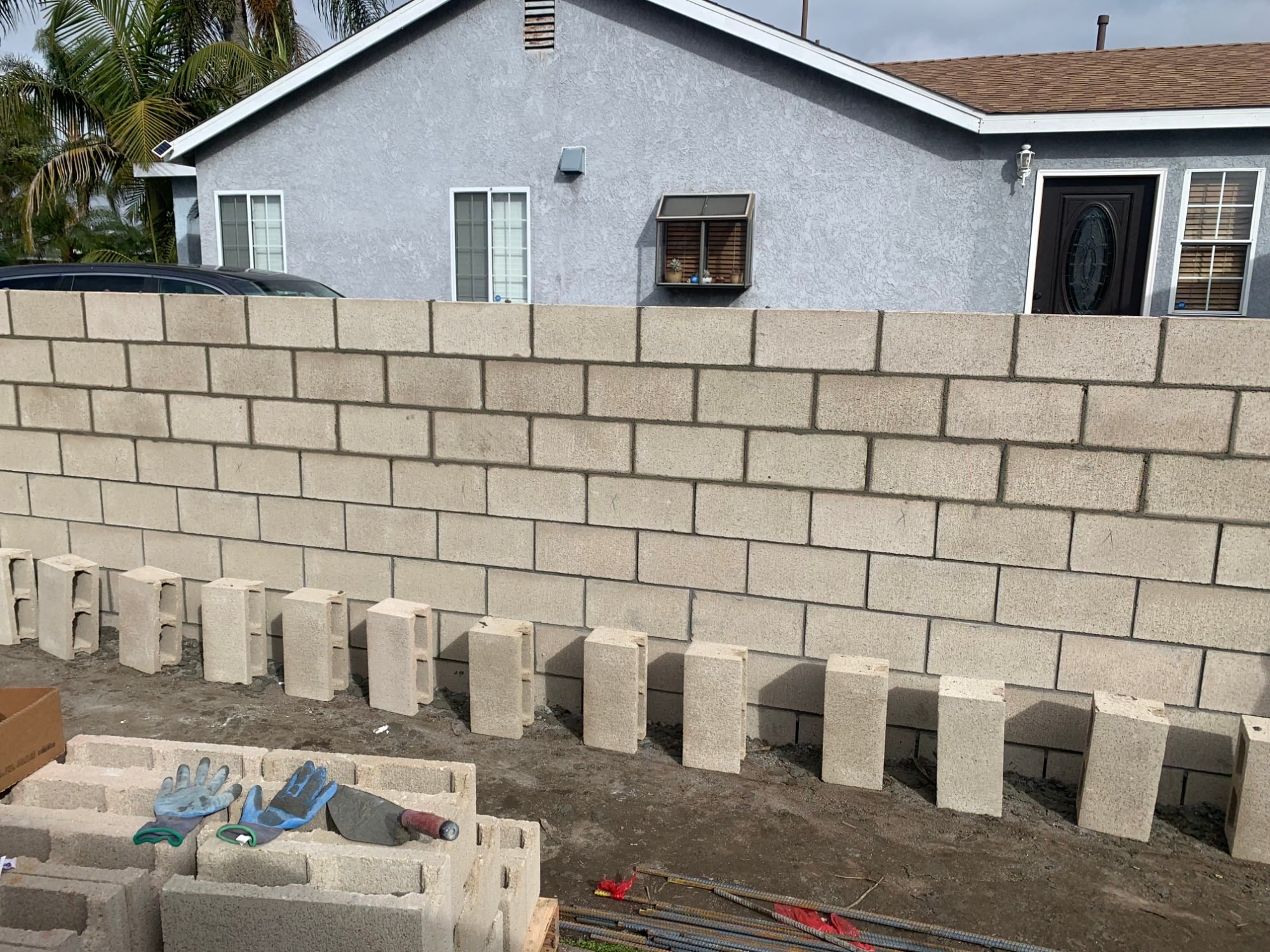 Concrete block wall under construction with rebar staged on site